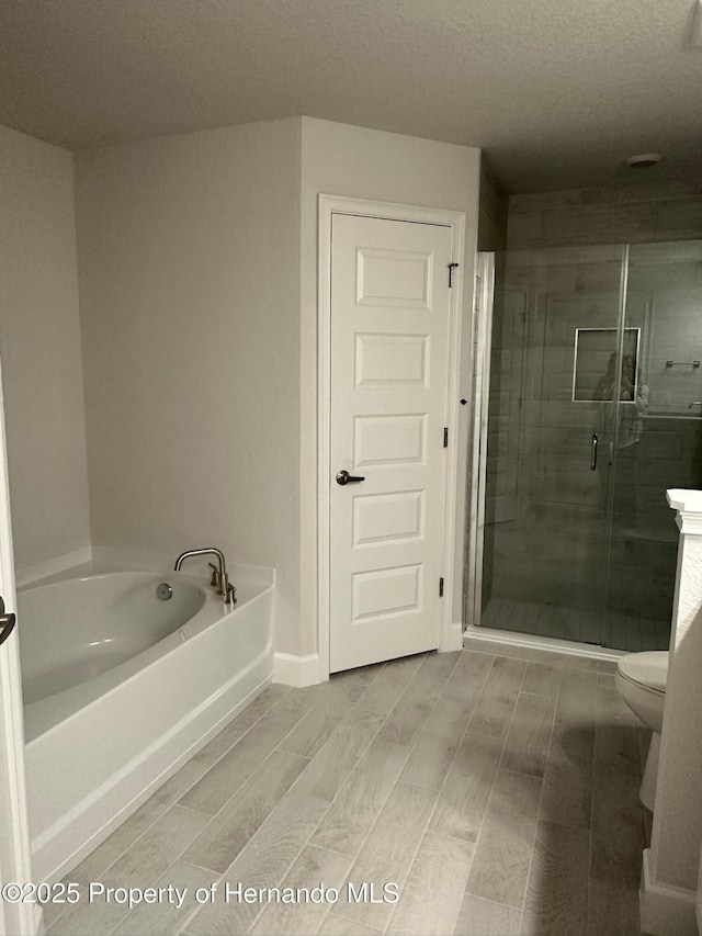 full bath featuring toilet, a textured ceiling, a shower stall, a bath, and wood tiled floor