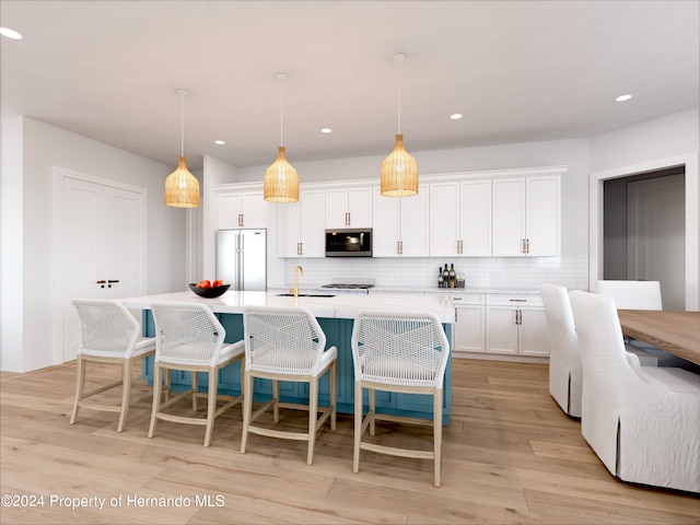 kitchen with white cabinets, hanging light fixtures, a center island with sink, and appliances with stainless steel finishes