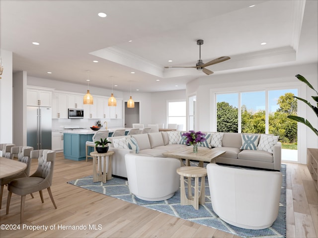 living room with light hardwood / wood-style flooring, ceiling fan, crown molding, and a tray ceiling