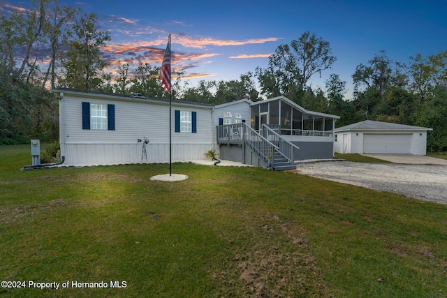 manufactured / mobile home with a sunroom, a garage, a lawn, and an outdoor structure