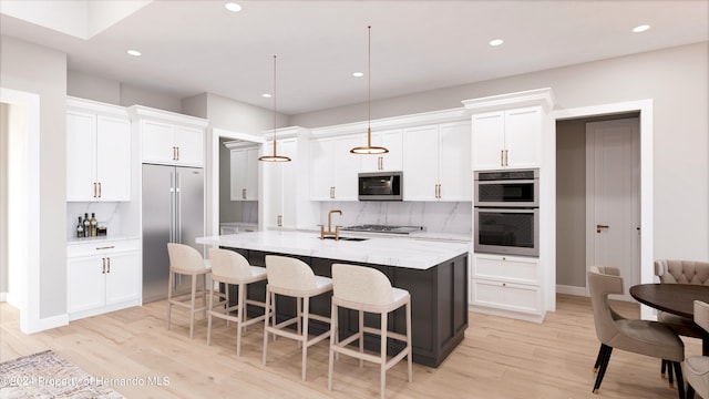 kitchen featuring white cabinets, a kitchen island with sink, light stone countertops, pendant lighting, and appliances with stainless steel finishes