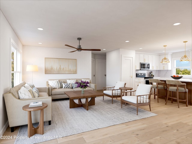 living room with ceiling fan with notable chandelier and light hardwood / wood-style flooring