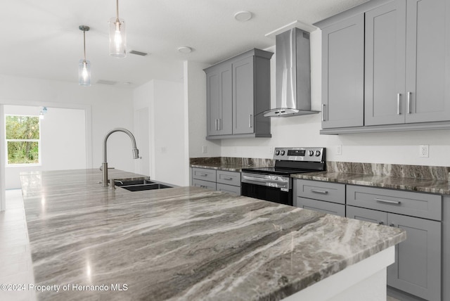 kitchen with stainless steel electric range, sink, wall chimney range hood, decorative light fixtures, and dark stone countertops