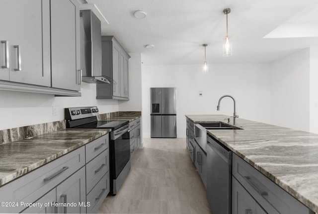 kitchen with hanging light fixtures, gray cabinetry, wall chimney range hood, light stone countertops, and appliances with stainless steel finishes