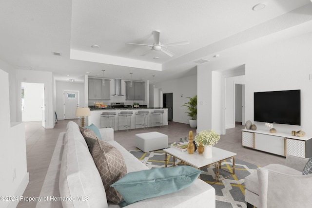 tiled living room with ceiling fan and a raised ceiling