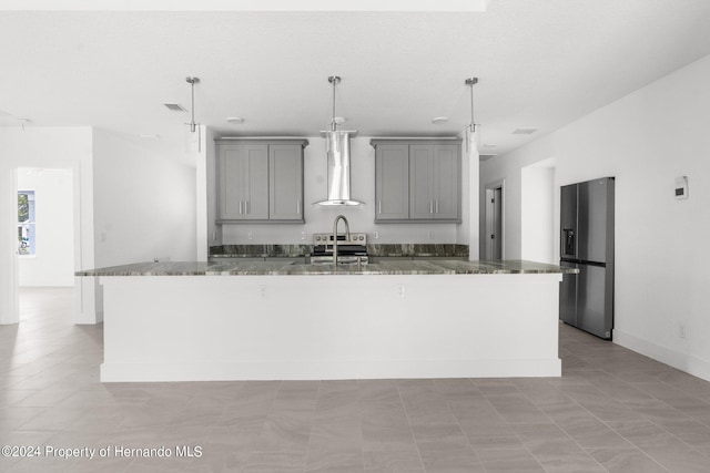 kitchen featuring stainless steel appliances, hanging light fixtures, gray cabinetry, a kitchen island with sink, and wall chimney range hood