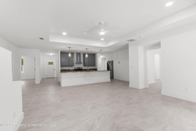 kitchen with gray cabinets, wall chimney exhaust hood, ceiling fan, and a raised ceiling