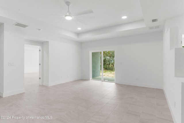 empty room with ceiling fan and a raised ceiling