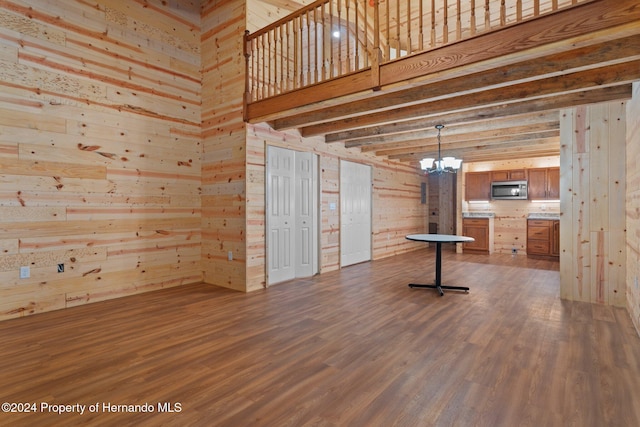 unfurnished living room with dark hardwood / wood-style flooring, wood walls, and a chandelier