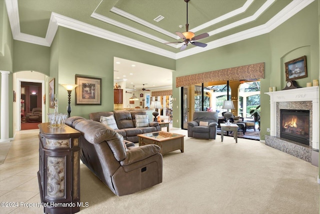 living room featuring a high ceiling, ceiling fan, a fireplace, a raised ceiling, and crown molding