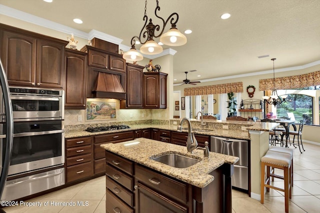 kitchen featuring premium range hood, a center island with sink, appliances with stainless steel finishes, pendant lighting, and sink