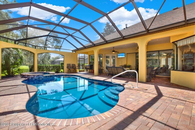 view of swimming pool with an in ground hot tub, ceiling fan, a patio, outdoor lounge area, and glass enclosure