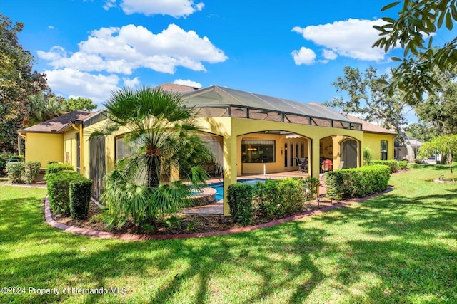 back of property featuring a lawn, ceiling fan, glass enclosure, and a patio area