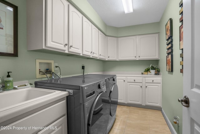 laundry area with cabinets, a textured ceiling, light tile patterned floors, and washer and clothes dryer