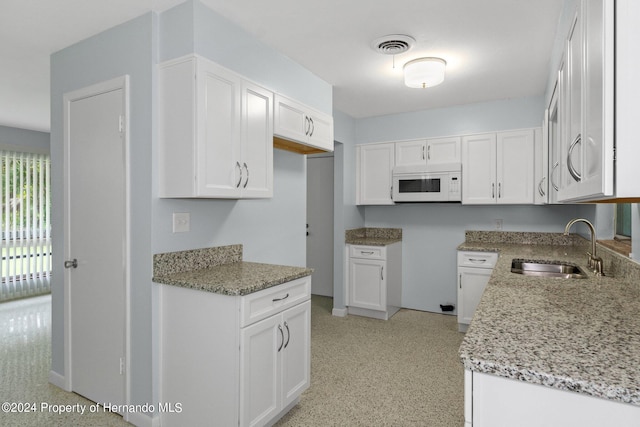 kitchen with white cabinetry, sink, and light stone counters