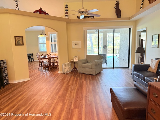 living room with ceiling fan, a wealth of natural light, wood-type flooring, and a towering ceiling