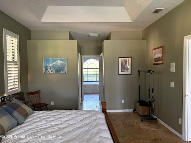 bedroom with a textured ceiling, multiple windows, and a tray ceiling