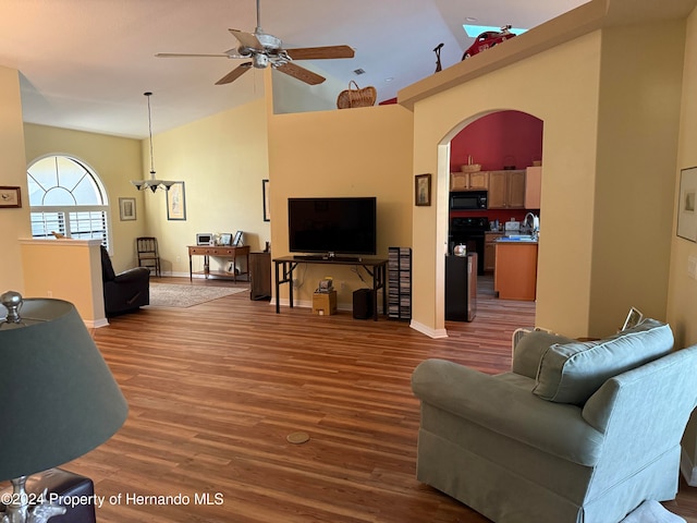 living room with wood-type flooring, ceiling fan with notable chandelier, sink, and high vaulted ceiling