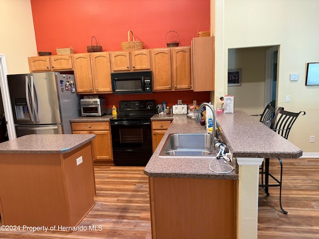 kitchen with kitchen peninsula, light hardwood / wood-style floors, black appliances, and sink