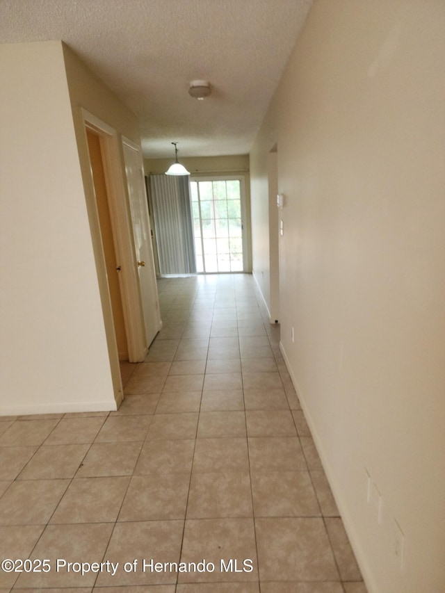 corridor with light tile patterned flooring, a textured ceiling, and baseboards