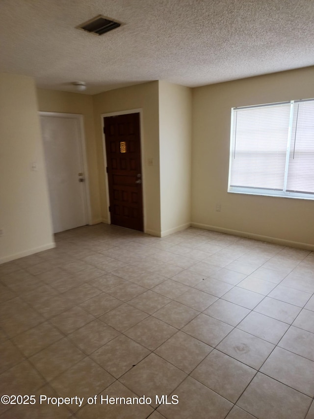 spare room featuring a textured ceiling, visible vents, and baseboards