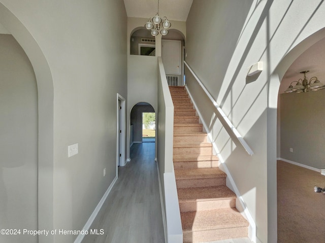 stairway featuring wood-type flooring, a notable chandelier, and a towering ceiling