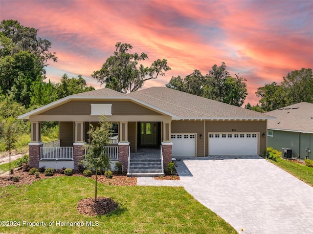 view of front of home with a garage, cooling unit, covered porch, and a lawn