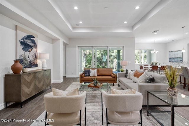 living room with hardwood / wood-style floors, a tray ceiling, and an inviting chandelier