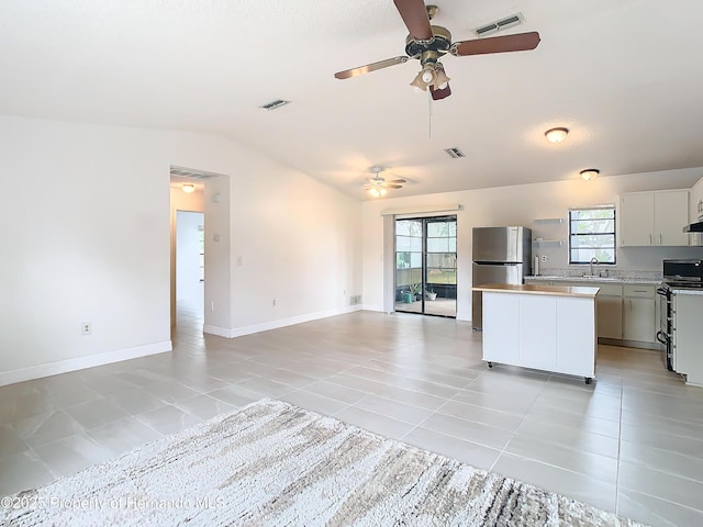 kitchen featuring stove, white cabinets, light tile patterned floors, a healthy amount of sunlight, and stainless steel refrigerator