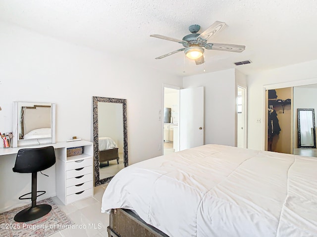 tiled bedroom featuring ceiling fan, ensuite bath, a textured ceiling, and a closet