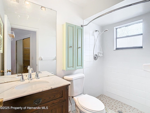 bathroom with a tile shower, vanity, and toilet