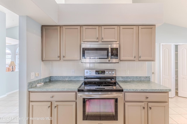 kitchen featuring vaulted ceiling, light tile patterned floors, decorative backsplash, and appliances with stainless steel finishes