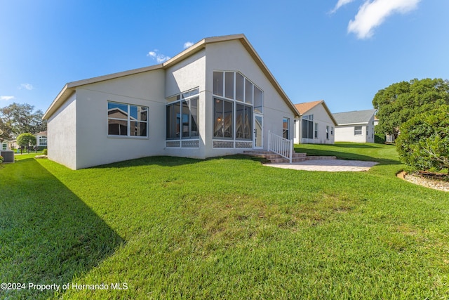 rear view of property featuring a patio, a sunroom, and a lawn