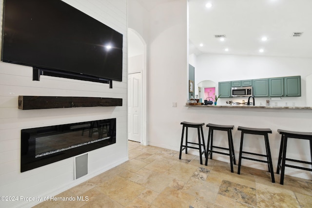 kitchen featuring sink, high vaulted ceiling, kitchen peninsula, a kitchen bar, and green cabinetry