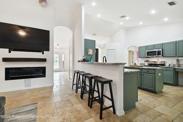 kitchen featuring kitchen peninsula, stainless steel appliances, high vaulted ceiling, a breakfast bar area, and green cabinets