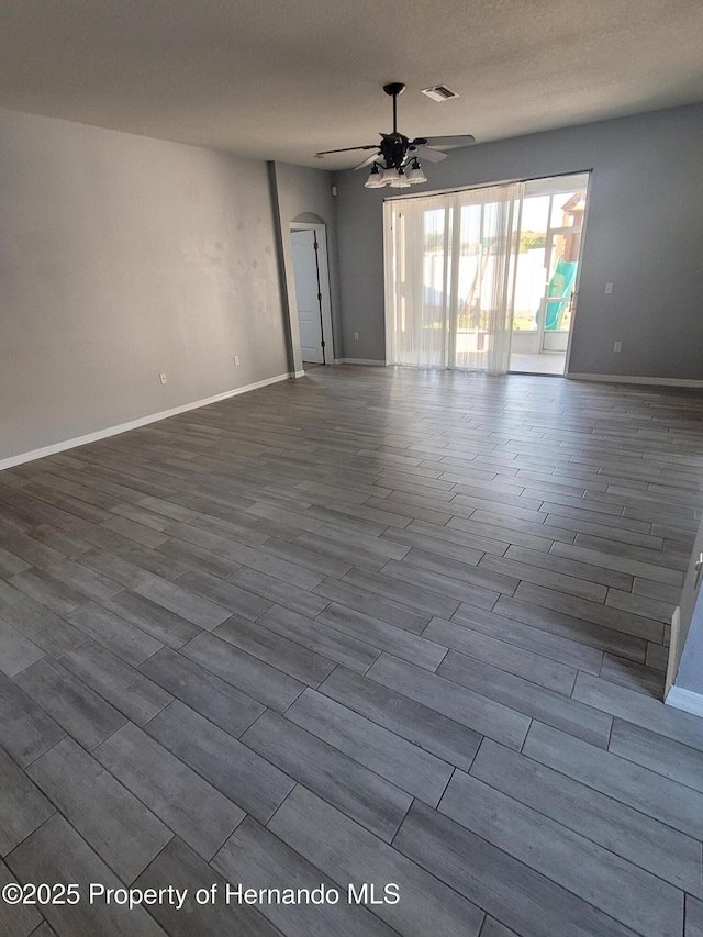 unfurnished room featuring arched walkways, dark wood-style floors, visible vents, and a ceiling fan
