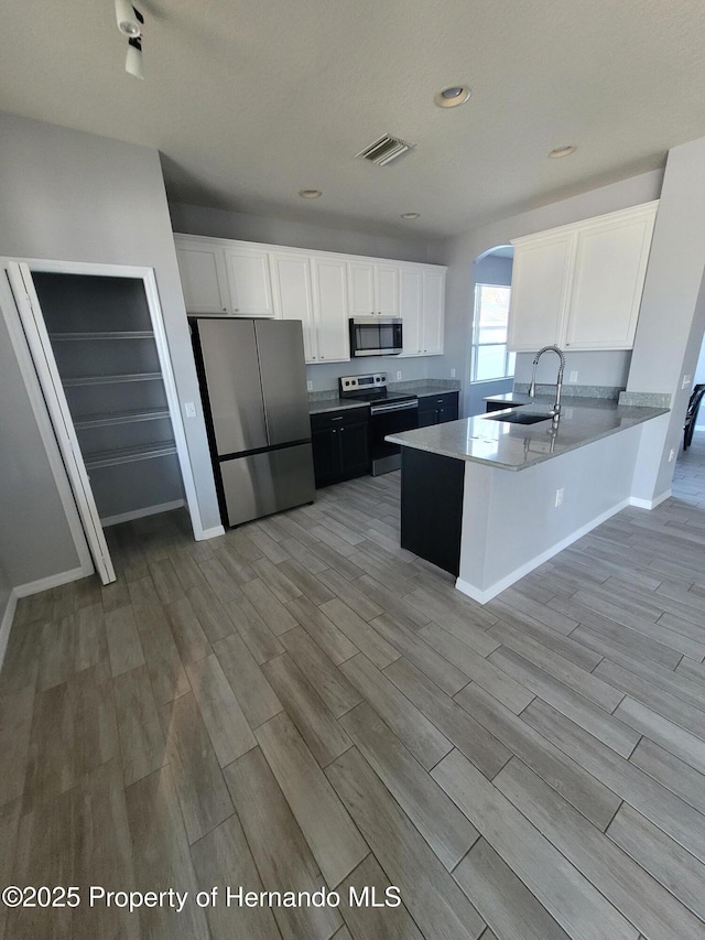 kitchen featuring arched walkways, stainless steel appliances, a sink, and white cabinets