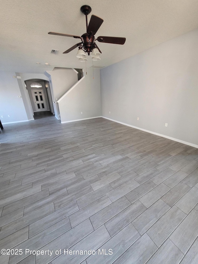 unfurnished living room with baseboards, visible vents, arched walkways, and wood finish floors