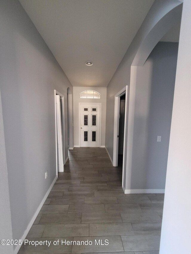 hall featuring baseboards, arched walkways, and wood finish floors