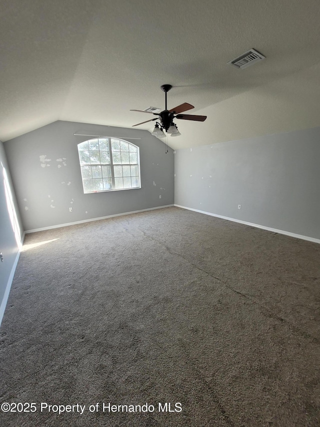 unfurnished room featuring baseboards, visible vents, vaulted ceiling, a textured ceiling, and carpet flooring