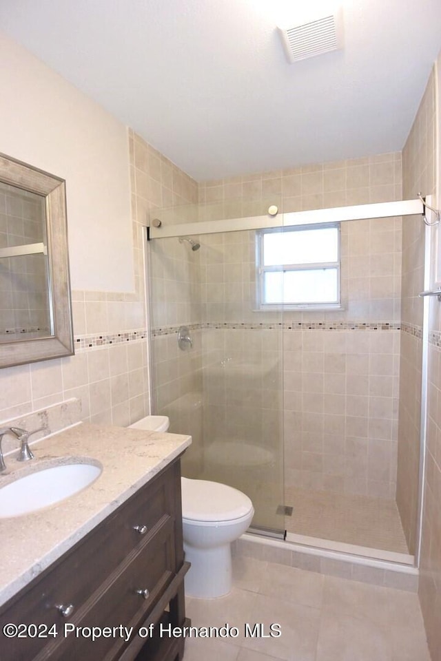 bathroom featuring walk in shower, tile patterned flooring, toilet, vanity, and tile walls