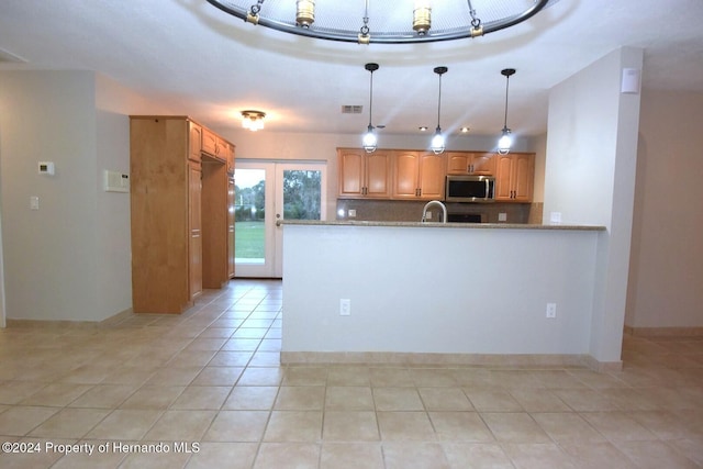 kitchen with hanging light fixtures, decorative backsplash, light stone countertops, light tile patterned floors, and kitchen peninsula