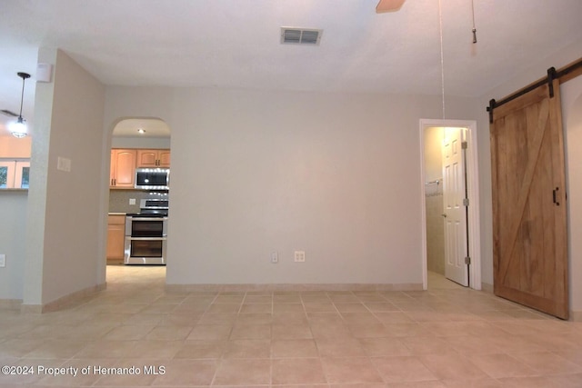 unfurnished room featuring light tile patterned floors, a barn door, and ceiling fan