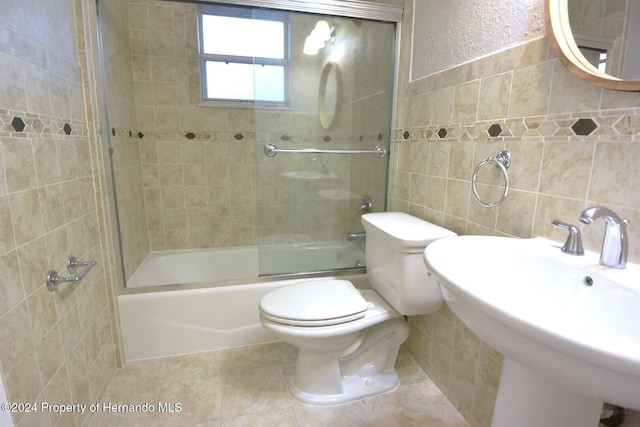 full bathroom with tile patterned floors, sink, shower / bath combination with glass door, tile walls, and toilet