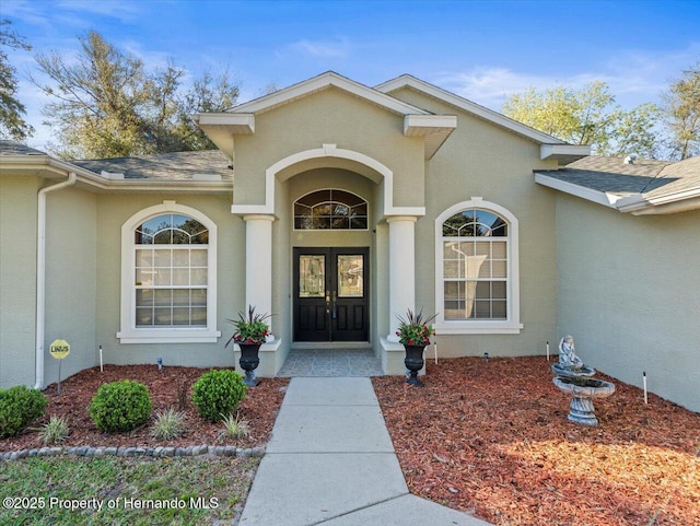 view of exterior entry featuring a shingled roof, french doors, and stucco siding