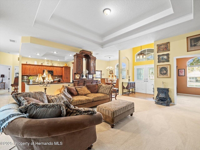 living area featuring french doors, a raised ceiling, light colored carpet, visible vents, and an inviting chandelier