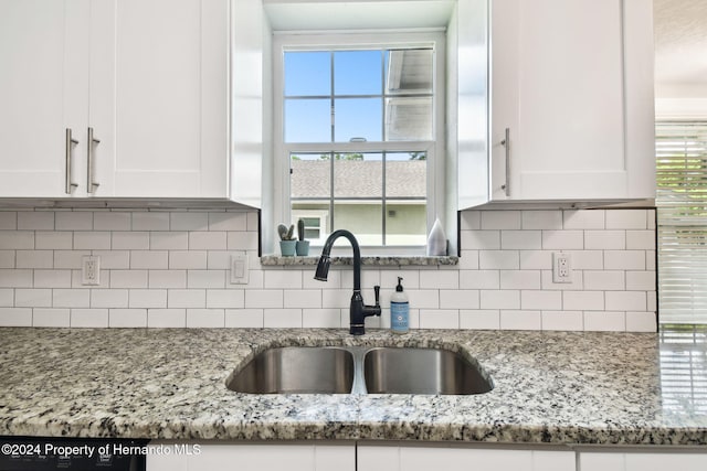 kitchen with white cabinets, decorative backsplash, light stone counters, and sink