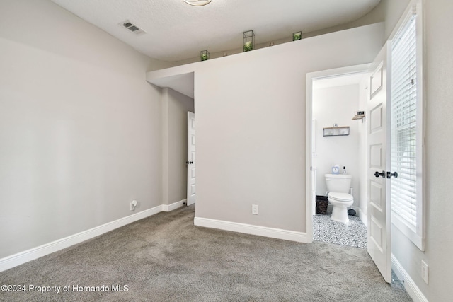 unfurnished bedroom with ensuite bathroom, carpet, and a textured ceiling