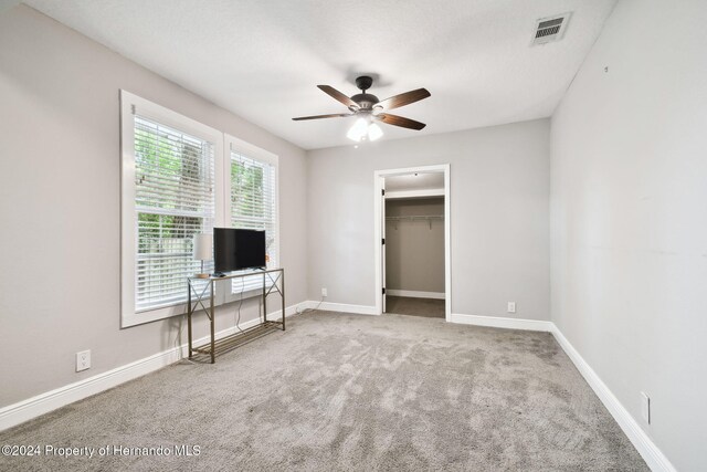 unfurnished bedroom featuring carpet, ceiling fan, a walk in closet, and a closet