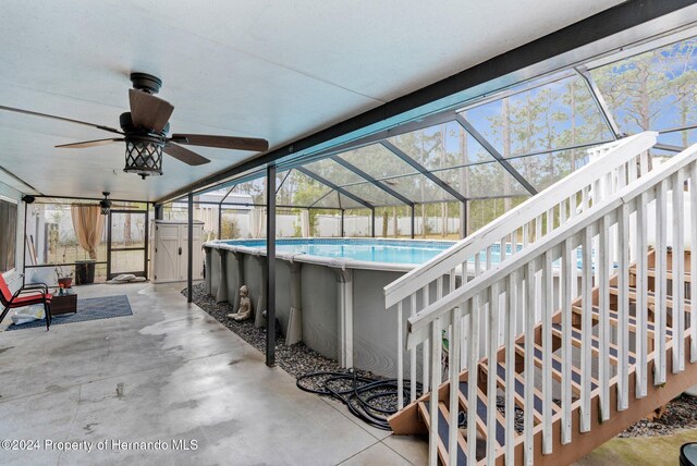 view of pool featuring glass enclosure, a shed, ceiling fan, and a patio area